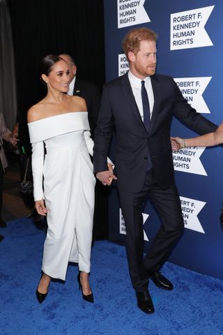 Meghan Markle wearing a white off the shoulder dress with Prince Harry