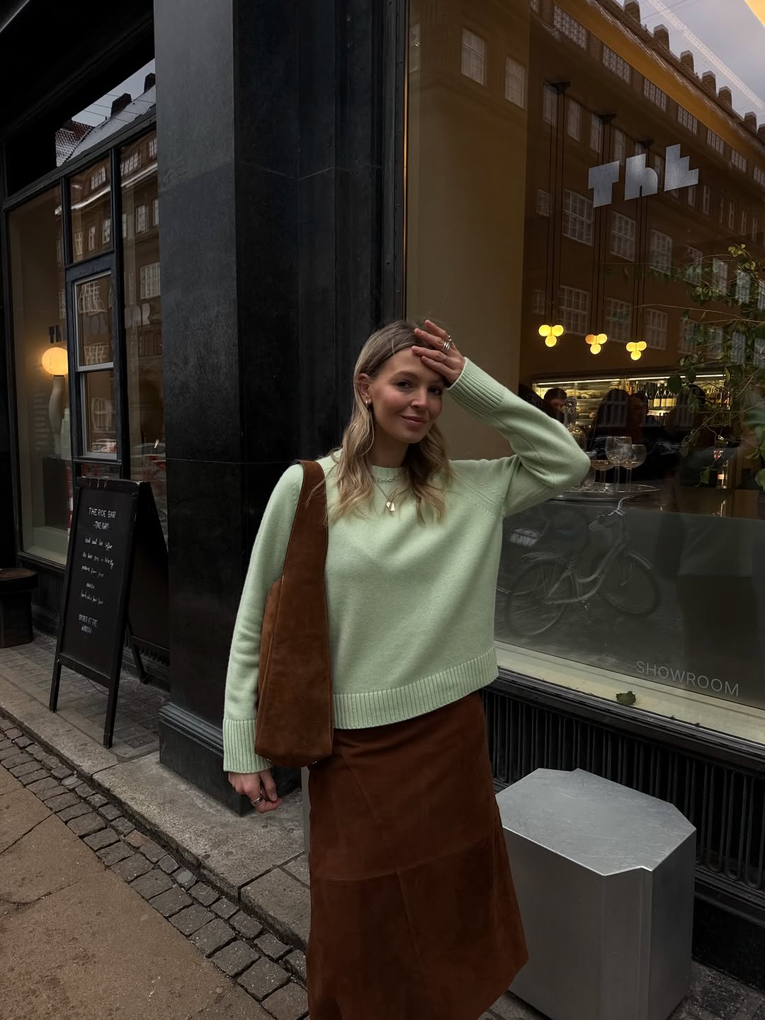 A woman wearing a pastel green sweater and brown suede skirt, one of the biggest 2026 spring color pairings.