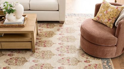 close up of patterned woven rug from Pottery Barn with timber coffee table styled with vases and woven tray, a white sofa, and a rust armchair with yellow cushion