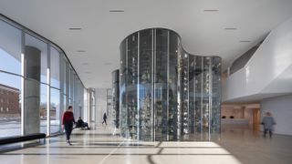 Interior foyet of the quamajuq inuit art centre, glass fronted casting shadows, glass design centre piece, visitors walking by, gloss neutral stone floor