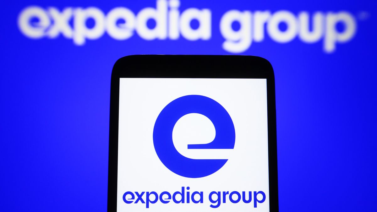 The Expedia Group Inc. logo shown on a smartphone in the foreground, and the words &quot;Expedia Group&quot; on a blue screen in the background. Decorative: The logo on the phone is displayed against a white background.