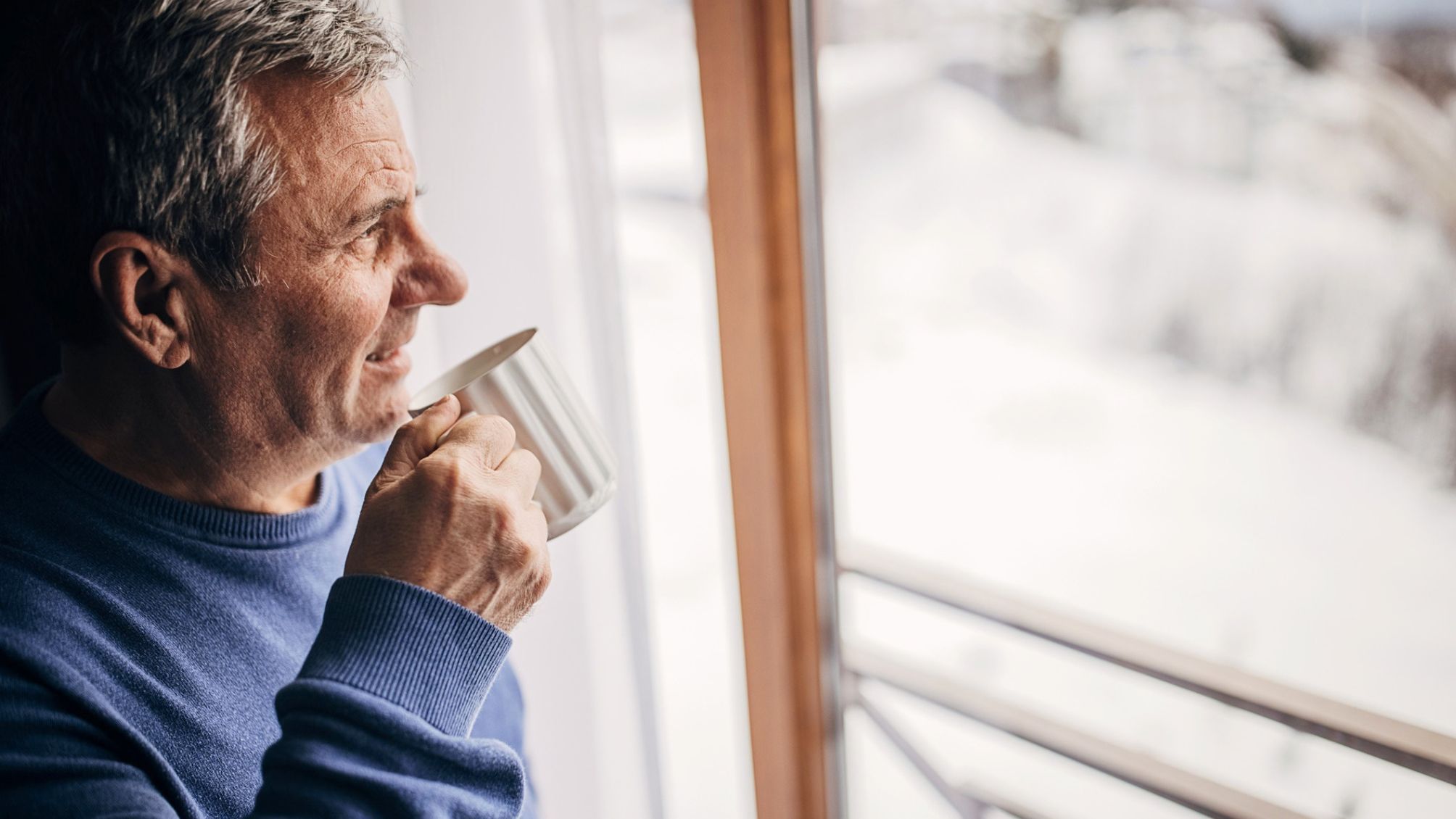 A man looking at snow fall from his cozy warm home. 
