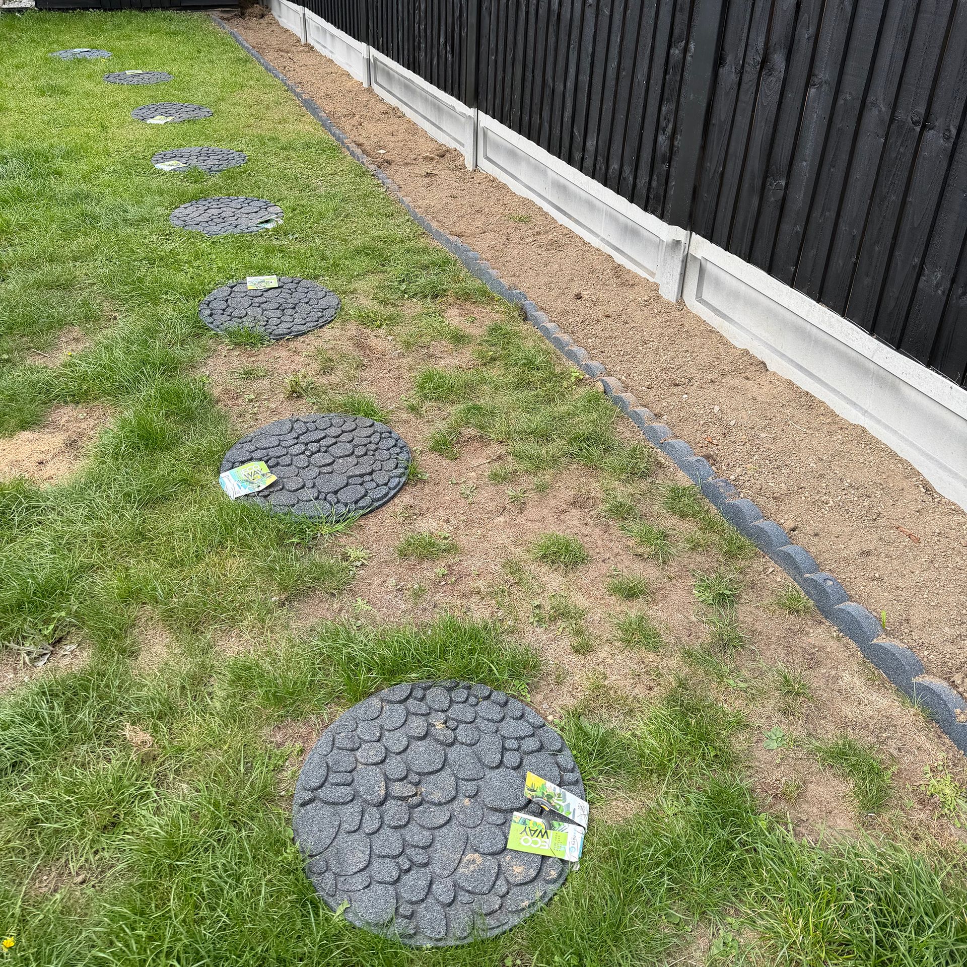 Round pebble patterned pavers in lawn by black fence