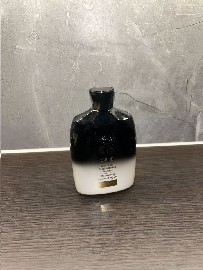 The Oribe Gold Lust Repair and Restore Shampoo on the side of a marble bathroom