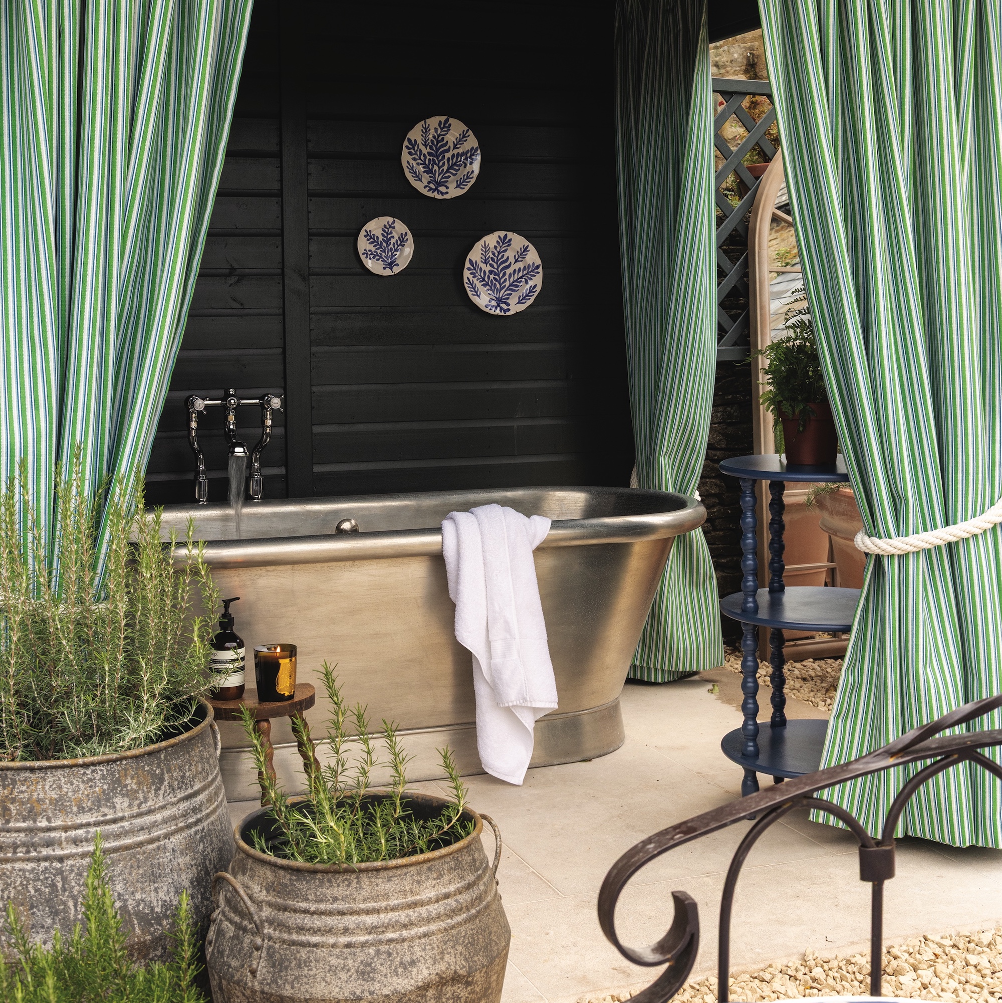 silver bath beneath black painted structure with green stripe curtains in garden