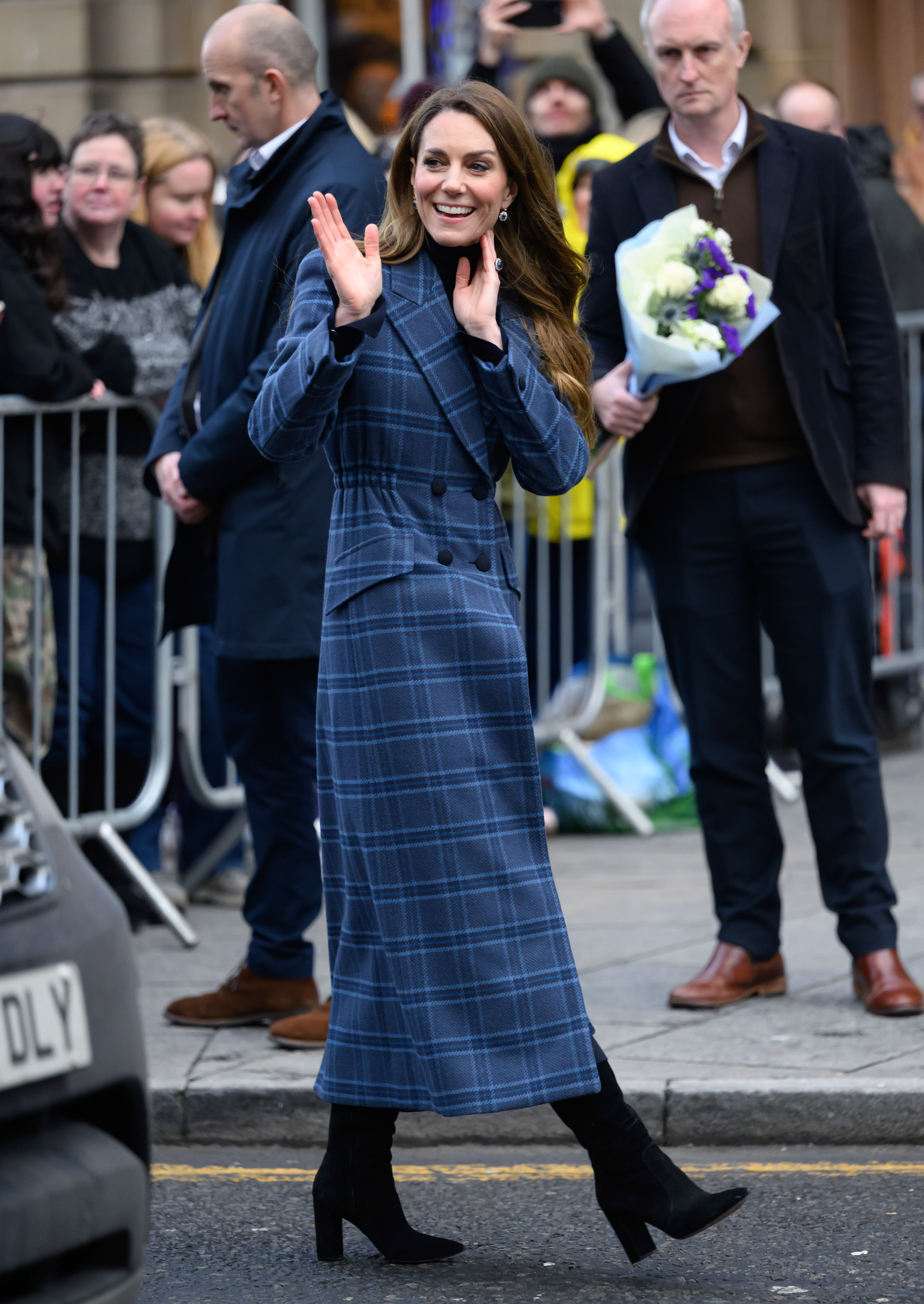Princess Kate wearing a blue plaid coat and waving in front of a group of fans