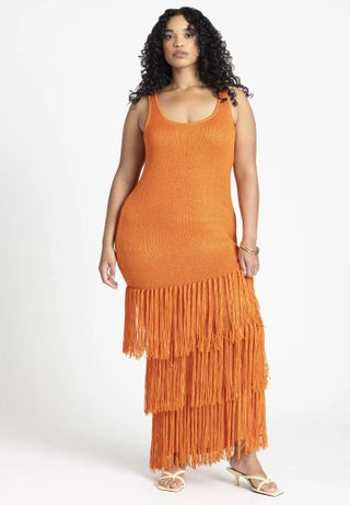 model wears orange dress with tiered fringe hemline and white heeled sandals