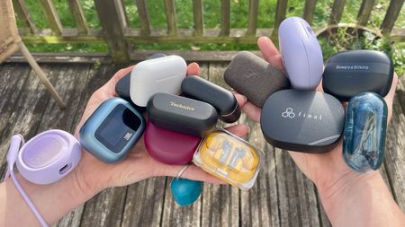 A selection of wireless earbuds, in their cases, held in a woman's hands on a sunny day