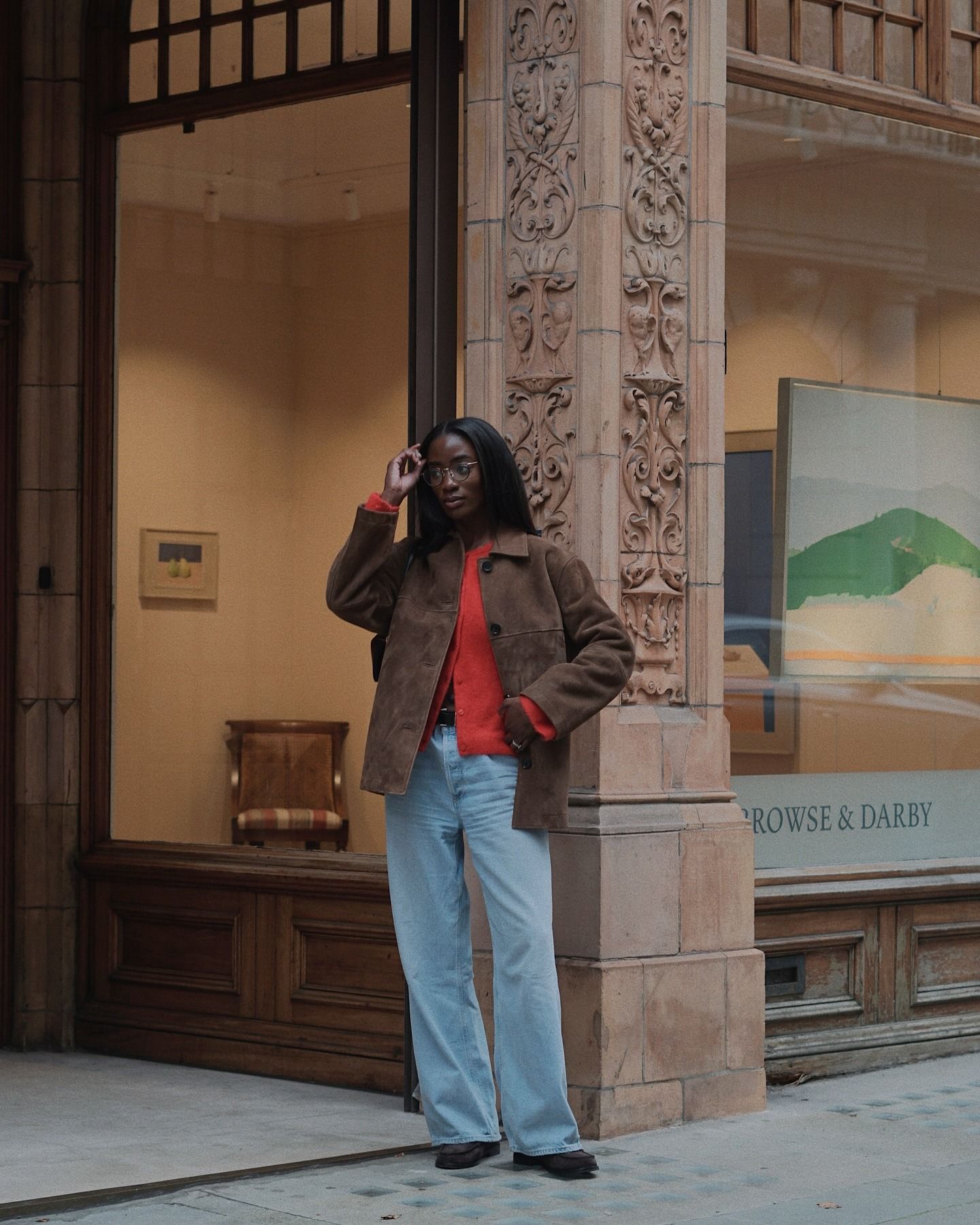 Liv wears a brown suede jacket, red cardigan, blue jeans