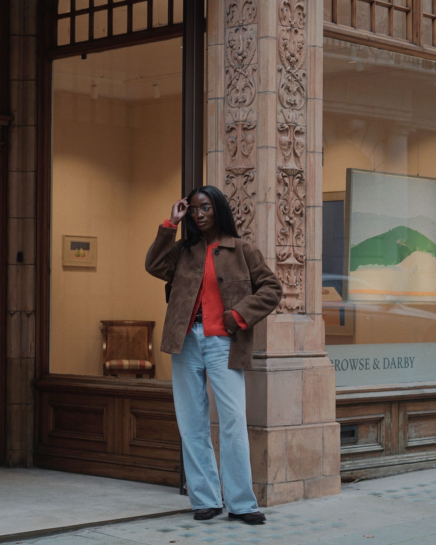 Liv wears a brown suede jacket, red cardigan, blue jeans