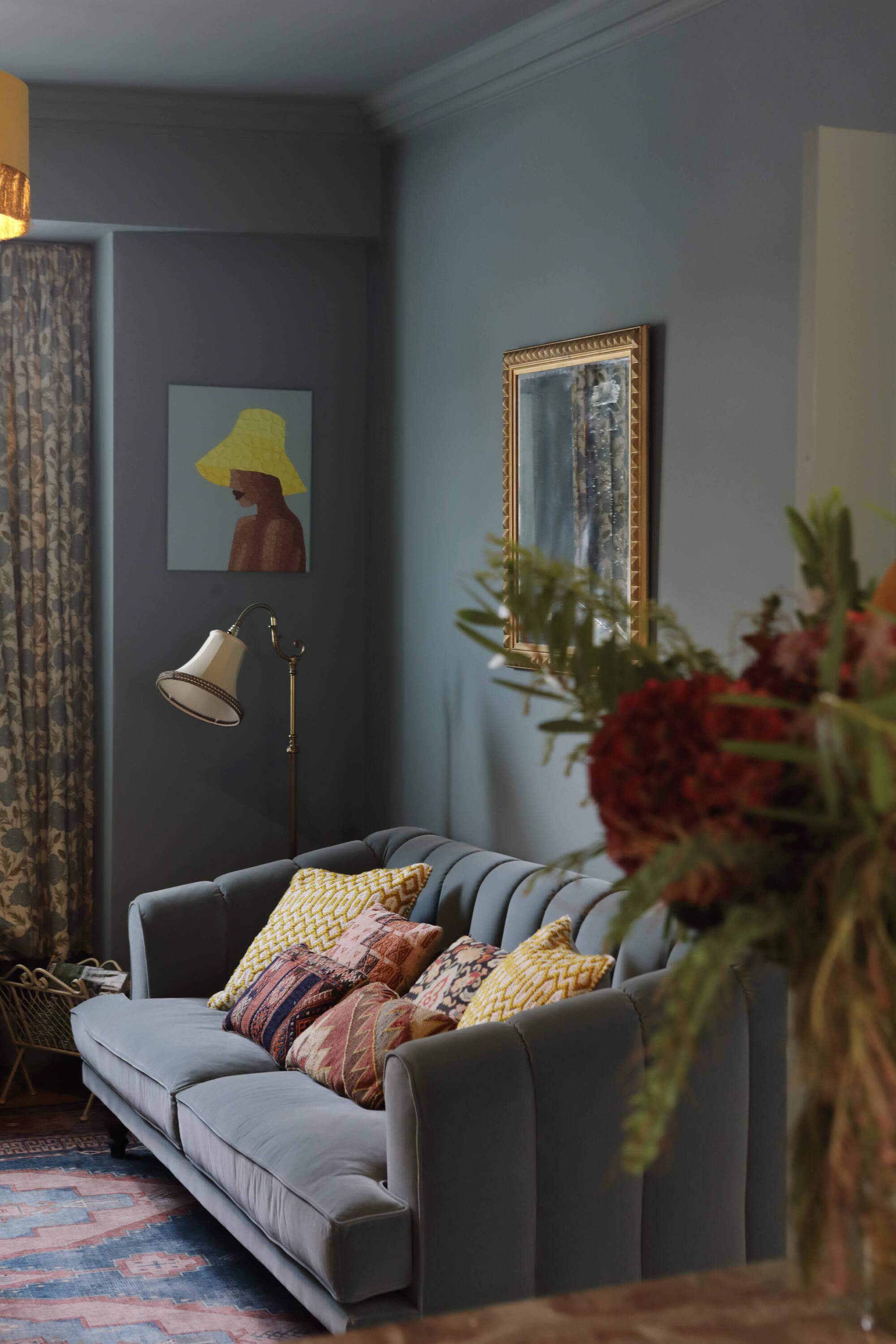 blue living room with blue sofa, artwork on the walls, patterned curtains and patterned rug, and vase of flowers in the foreground