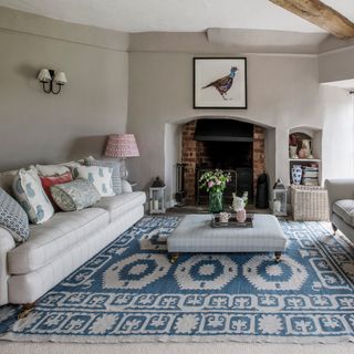 grey living room with a brick fire place and a grey striped sofa with patterned pillows and a striped material coffee table with accessories