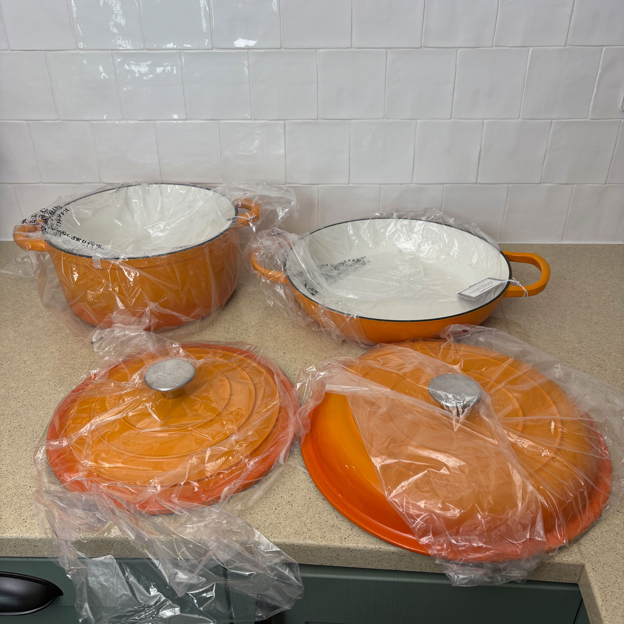 Orange cast iron pans in plastic wrapping on countertop