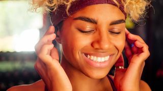 A woman holding wireless earbuds in her ears while smiling