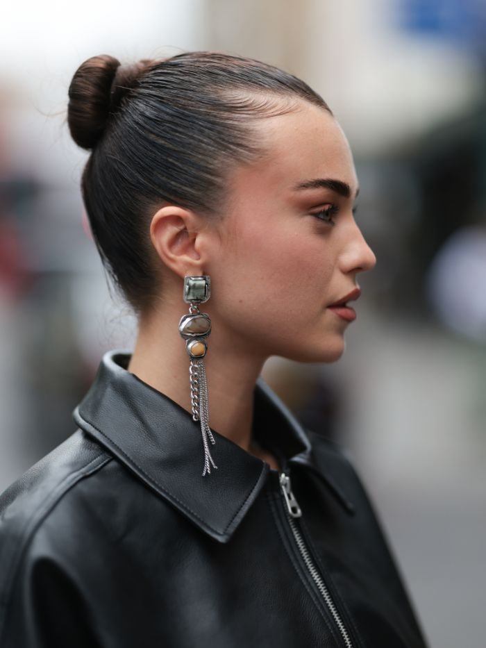 A woman at London Fashion Week wearing a black leather jacket with a slicked-back bun