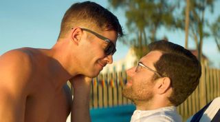 luke macfarlane leans into billy eichner sitting outside a pool in bros