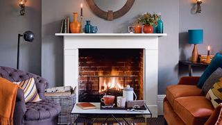 Gray living room with roaring open fire in fireplace with burnt orange and teal furniture and accessories