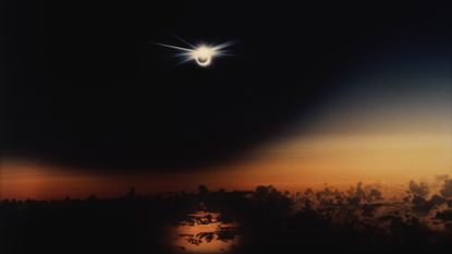 A solar eclipse over the Pacific Ocean at sunset, with the "diamond ring" feature visible.