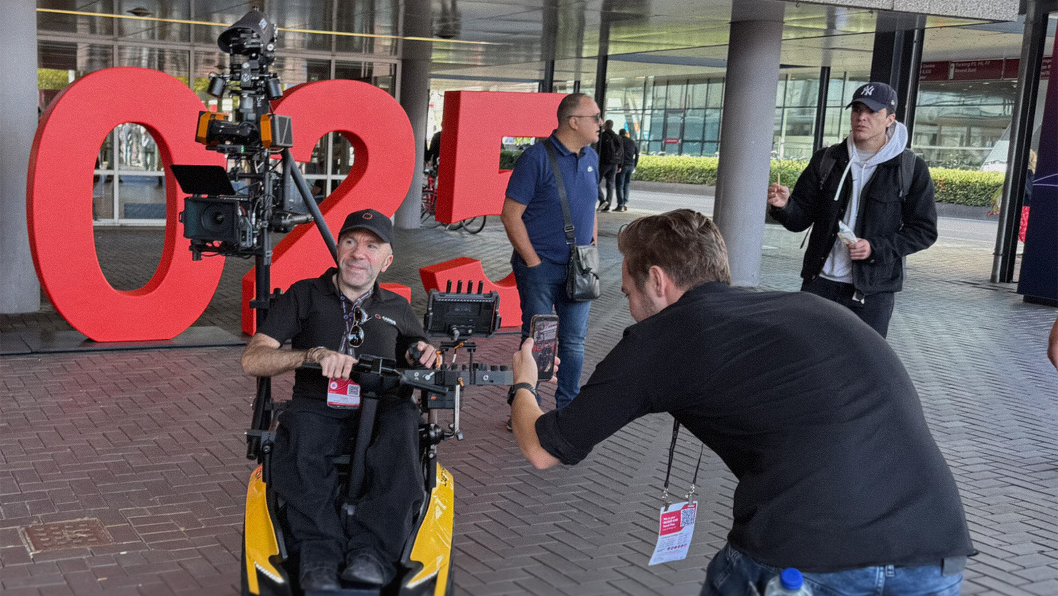 A man sits in a wheelchair housing a film camera rig. 