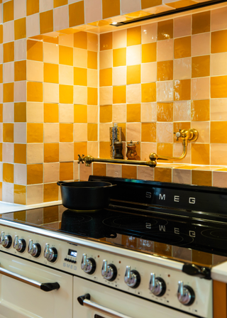 Yellow and white checkerboard backsplash for a retro, smeg oven with a built in hot water tap