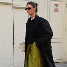 Influencer @cocoschiffer wears a chartreuse coloured skirt with white heels and a black wool coat.