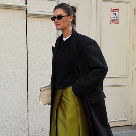 Influencer @cocoschiffer wears a chartreuse coloured skirt with white heels and a black wool coat.
