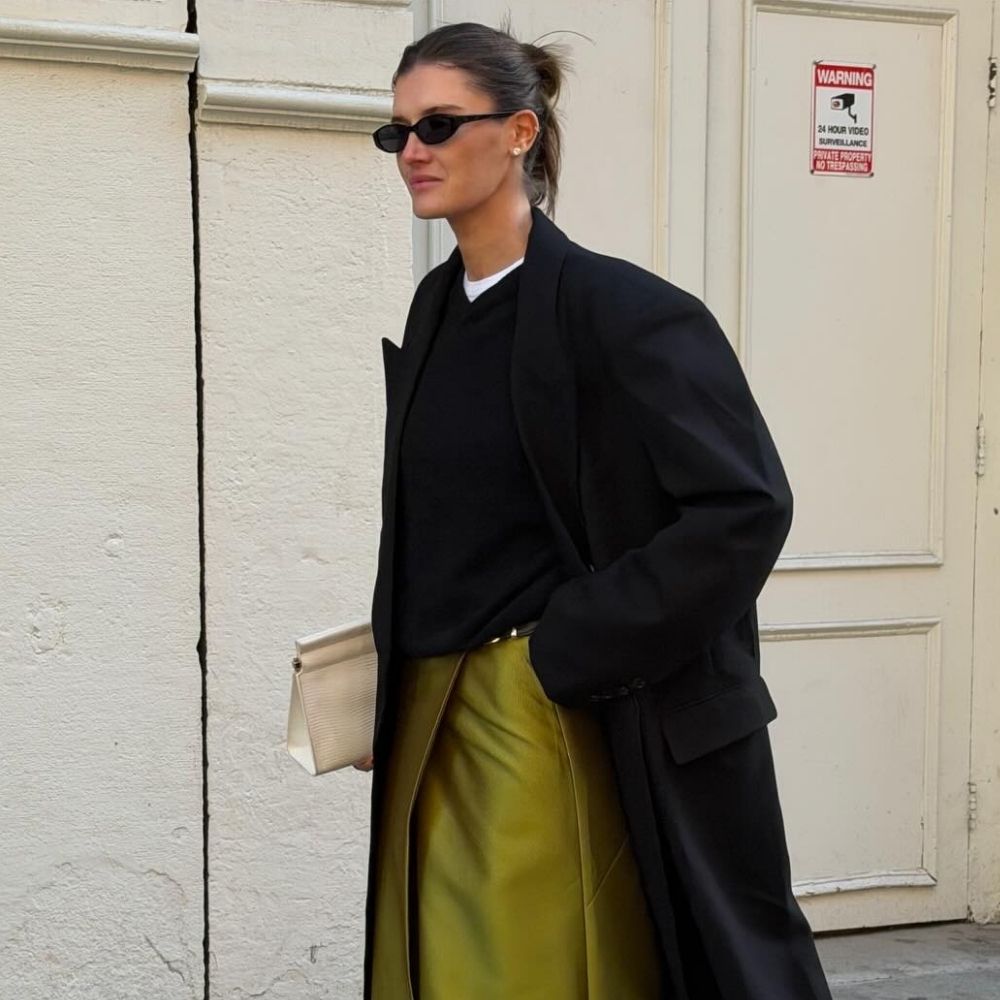 Influencer @cocoschiffer wears a chartreuse coloured skirt with white heels and a black wool coat.