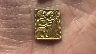 A person holds a tiny gold foil figure. 
