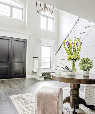 A white foyer with large black doors, double height ceilings and a brown wooden table