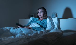 A young blonde woman watches tv in bed before she goes to sleep