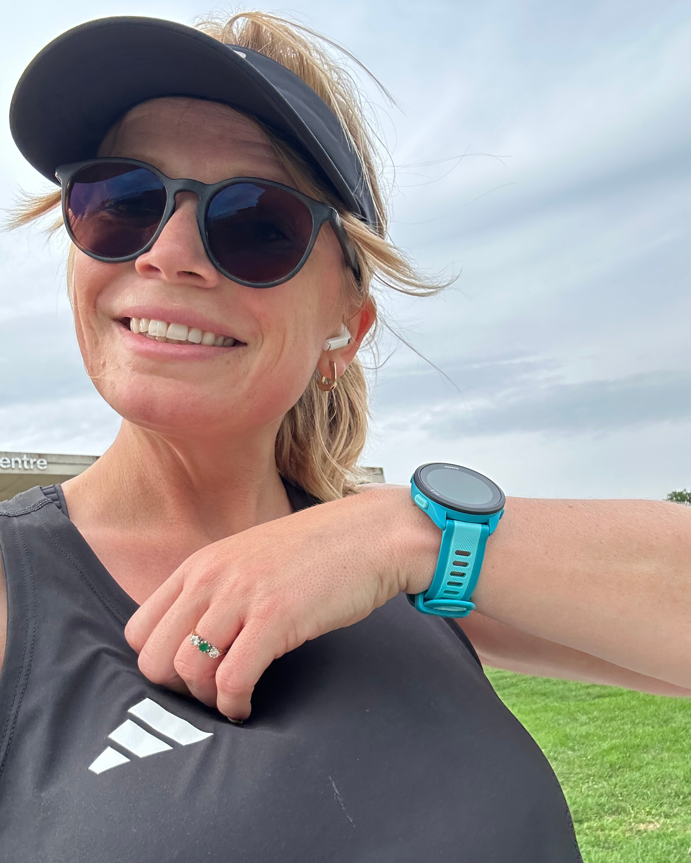 Woman wearing sunglasses and cap holds up her arm to show a turquoise watch