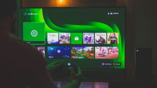 A person holding an Xbox controller in front of a bright screen showing off their games on the Xbox Dashboard