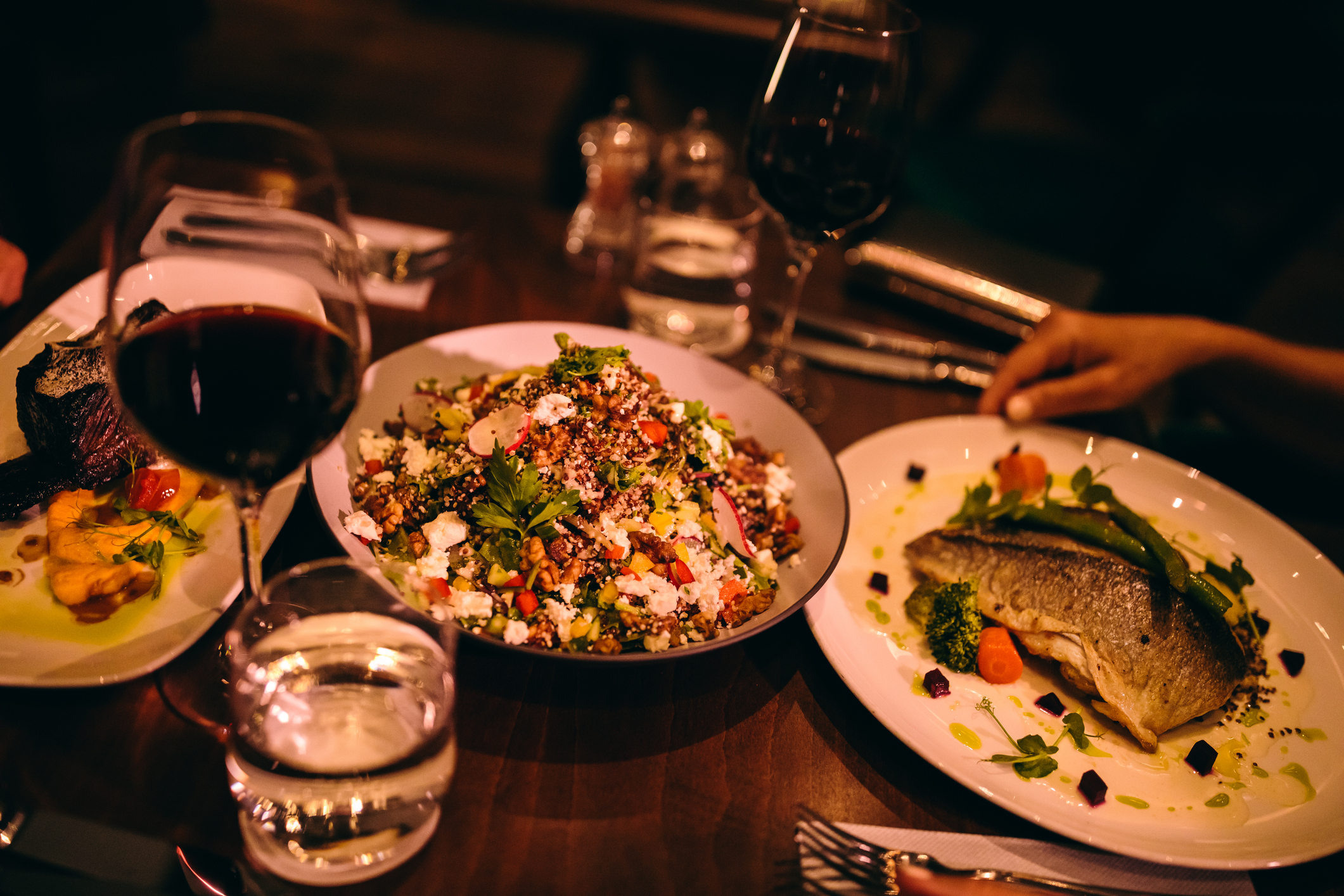 Main course dishes of fish, steak and salad served with red wine at gourmet restaurant in Cyprus.