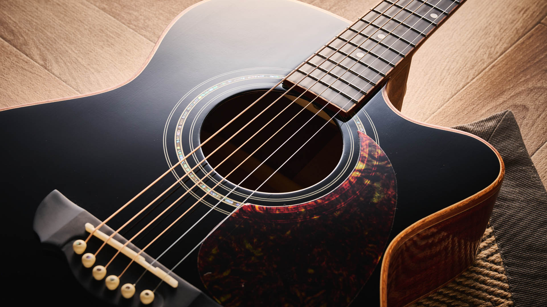 Harley Benton CLC-650SM-CE: the affordable cutaway electro-acoustic has a black top, natural back and sides, with an attractive arm-rest and tortoiseshell pickguard, and is here photographed against a wooden floor.