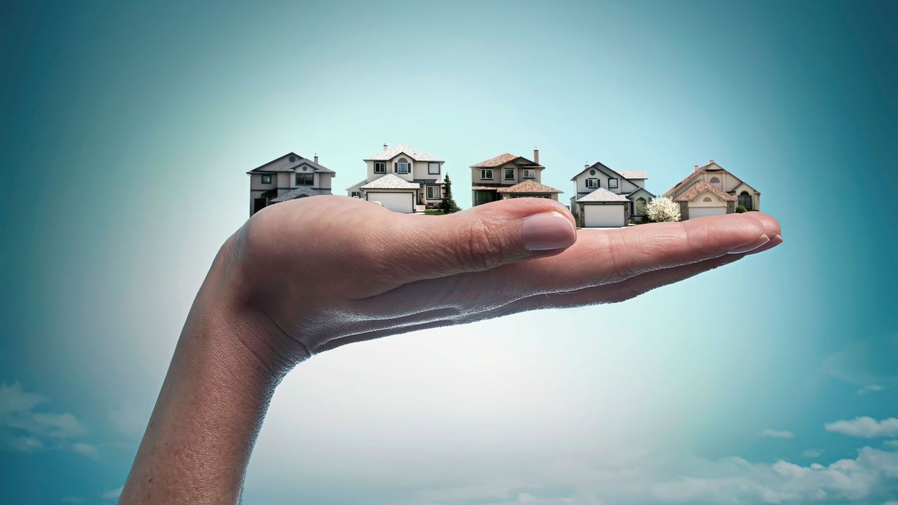 A hand holding several tiny models of homes