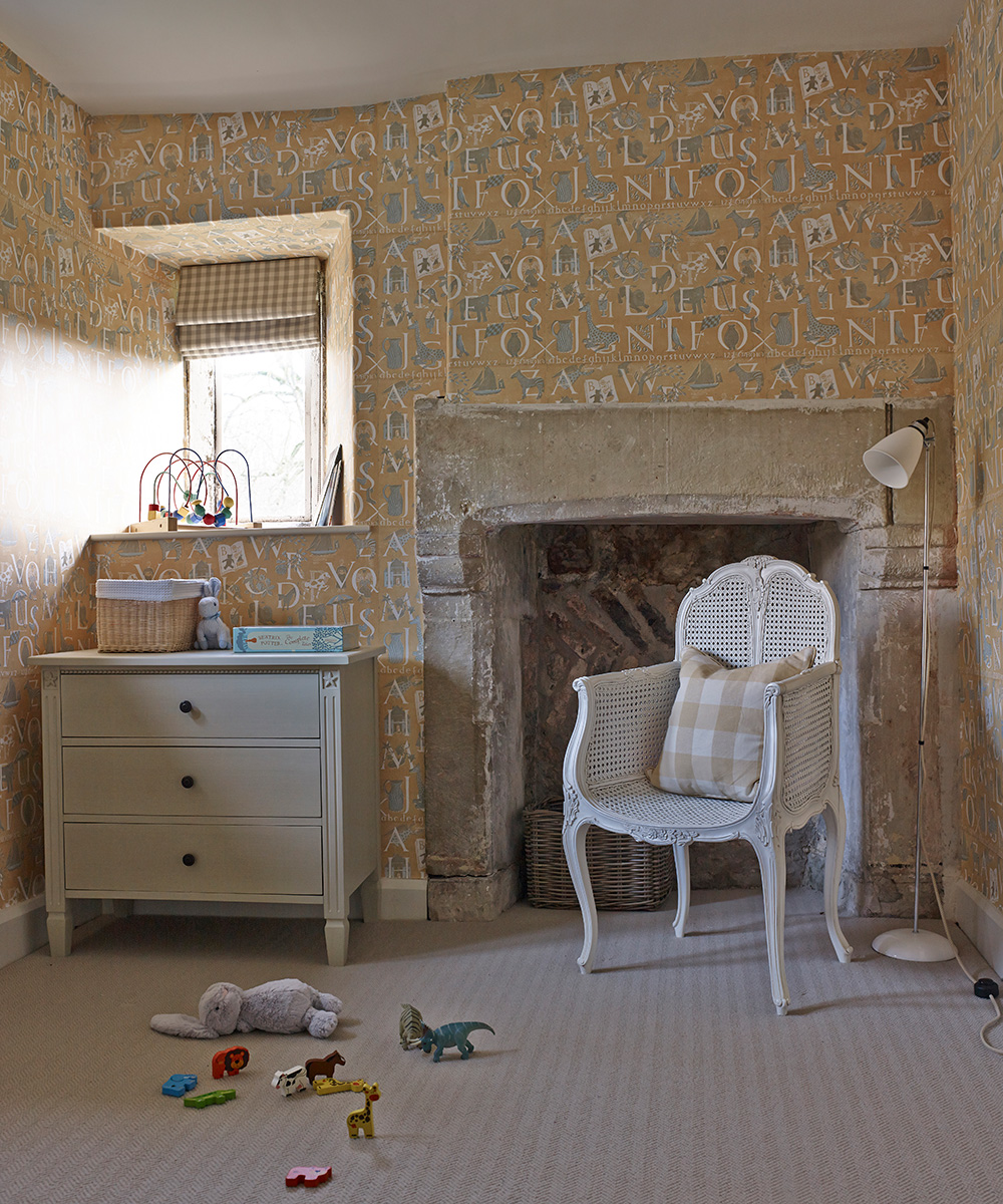 Alphabet-print wallpaper in a small bedroom idea for kids, with old stone fireplace and white wicker chair.