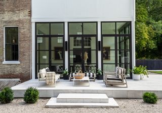 Paved patio outside black framed doors with white and grey sleek sofas and coffee table