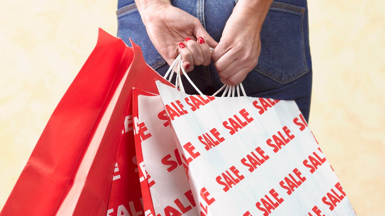 A woman holds several shopping bags with the words &amp;quot;sale&amp;quot; repeated in red on them.