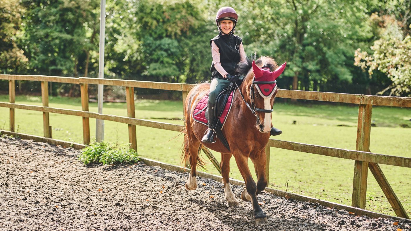 Young girl trots a bay pony toward the camera in a riding man&egrave;ge