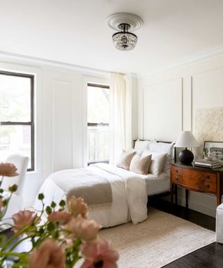 A studio apartment with paneled walls, a bed in the corner, and an antique-style side table