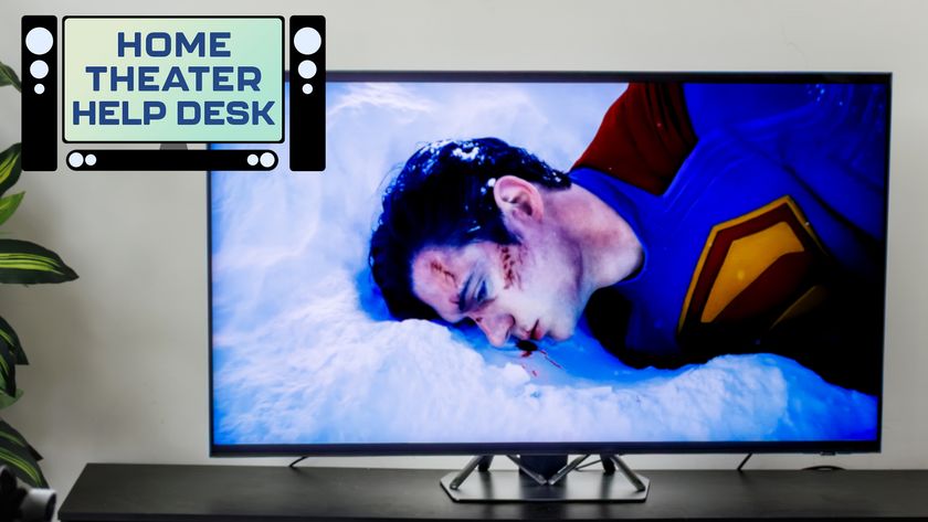 A TV on a credenza displaying a tattered, bloodied Superman from the 2025 movie "Superman." In the top-left corner of the image is a badge that reads: "Home Theater Help Desk."