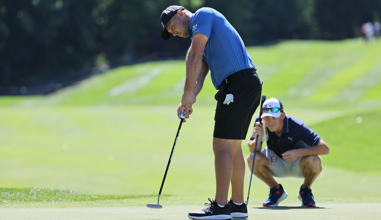 Bryson DeChambeau putts in shorts whilst someone squats behind him