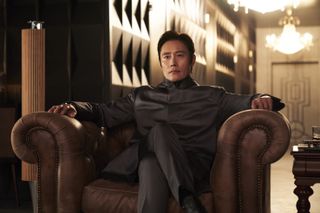 Lee Byung-hun as Front Man, sitting in a large leather armchair, in Squid Game S2