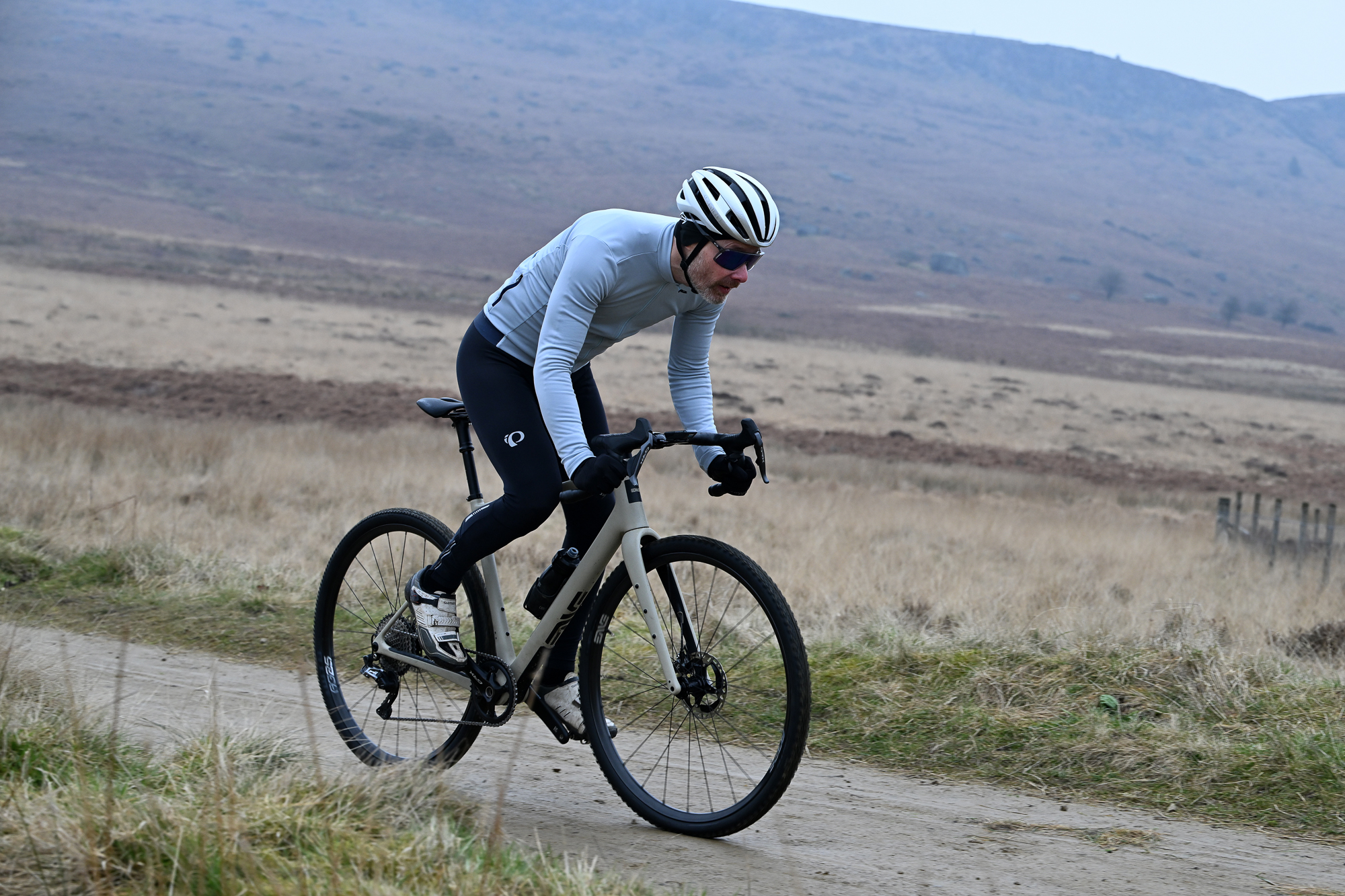 Man in a blue jersey riding a gravel bike on a sandy trail
