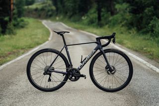 The full Orbea Orca bike side on a tarmac road with greenery either side