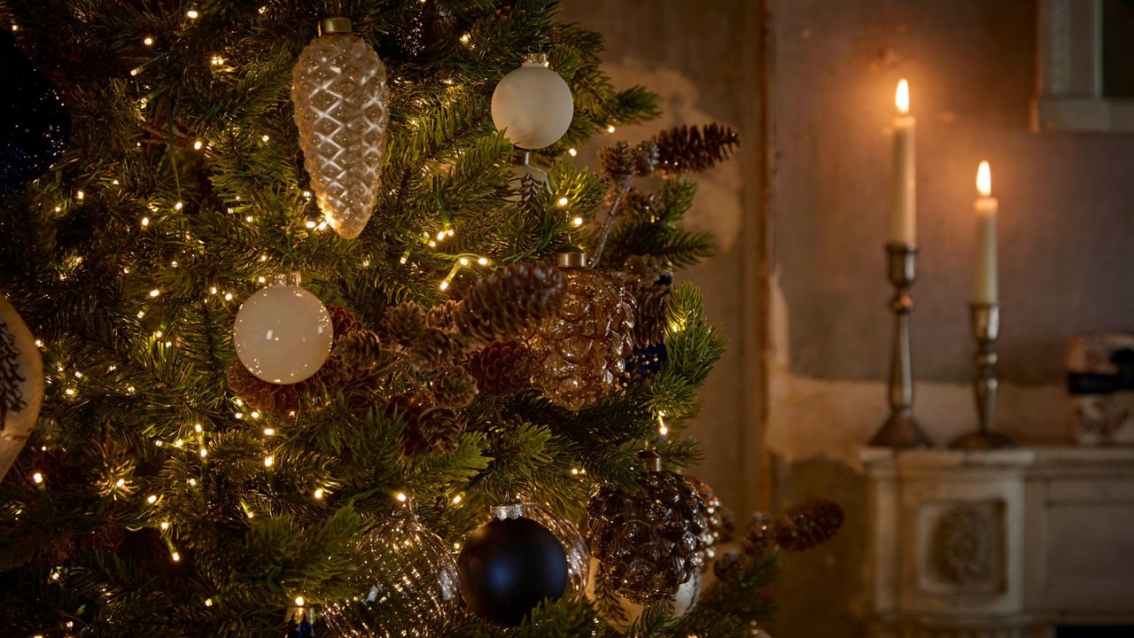 A close-up of a decorated Christmas tree by a mantel with lit tapers on holders