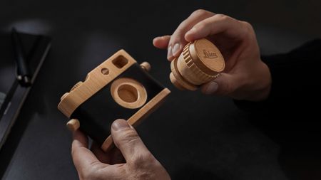 Wooden Leica camera with removable lens being held in person't hands indoors