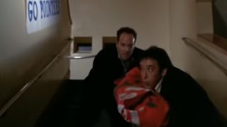 John Cusack and Jeremy Piven carrying a body wrapped in a banner down some stairs in Grosse Pointe Blank