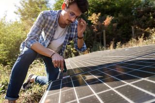 A man is seen adjusting a solar panel on the ground of his garden