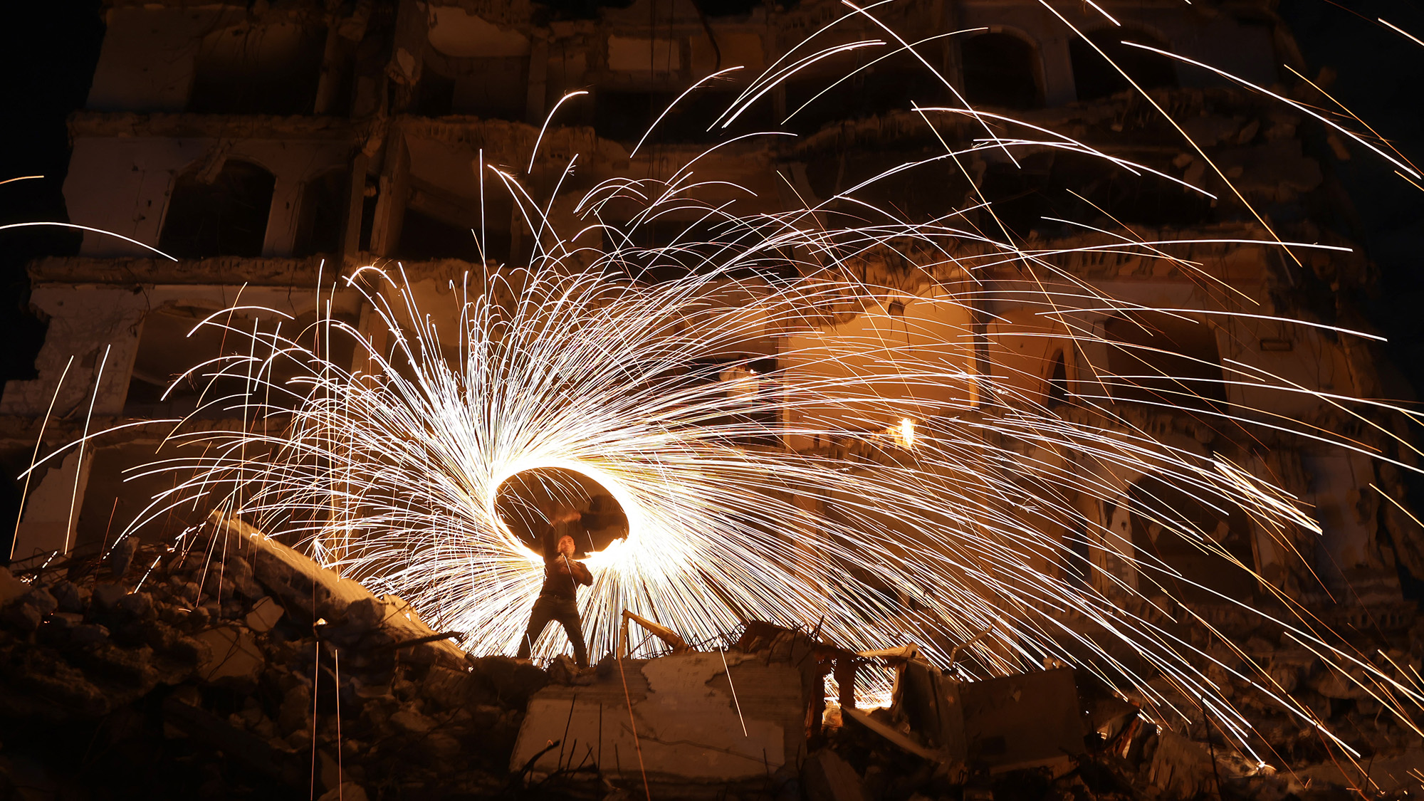 A displaced Palestinian plays with fireworks outside a building damaged by Israeli strikes at the Jabalia refugee camp, Palestine